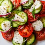 cucumber caprese salad served in a white bowl with tomatoes and basil